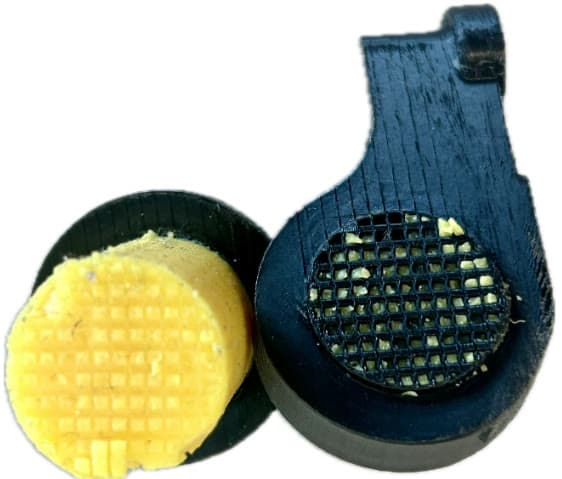 Photograph of a failed connector: the yellow silicone cylinder has separated from the black 3D-printed holder, exposing the checkerboard interlocking lattice.
